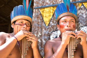 Native Brazilian guys playing wooden flute at an indigenous tribe in the Amazon